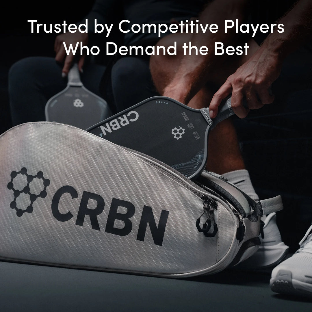 Person holding a pickleball paddle with CRBN branding, next to a CRBN racket bag.